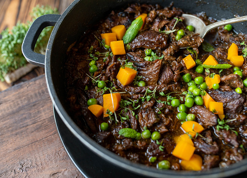 Homemade oven braised shredded beef with worcestershire sauce. Served ready to eat with peas and carrots in a pot on wooden background from above.
