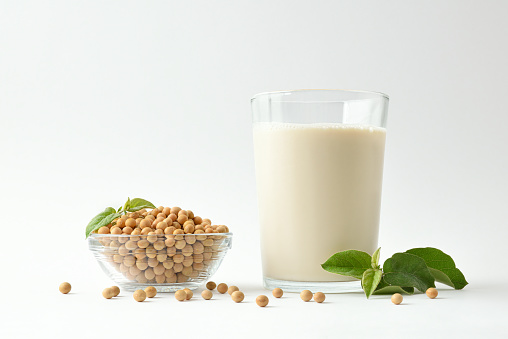 Background with glass cup with soy drink and bowl full of soy beans on white table isolated on white background. Front view.