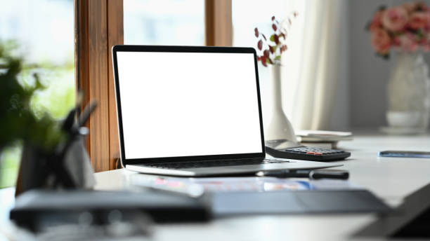 istock Laptop with blank display, coffee cup and stationery on white office desk. 1587007388