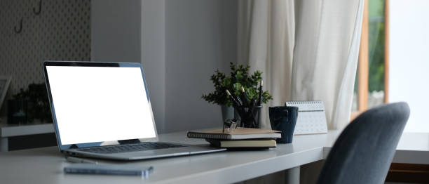 istock Laptop with blank display, coffee cup and stationery on white office desk. 1587008901