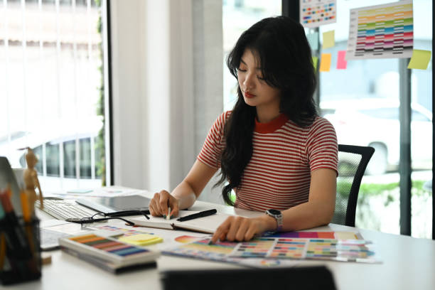 istock Young creative woman working with color palette, choosing color samples for design project at graphic studio. 1587012691