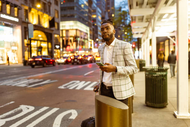 istock Affluent black businessman on a trip to NYC, using mobile phone app calling taxi 1587017609