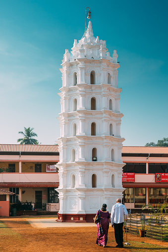 Kavlem, Phonda, Goa, India - February 20, 2020: People Walking Near Shree Shantadurga Mandir, Kavlem Temple. Famous Landmark And Popular Destination. White Lamp Tower. Shantadurga Devi.