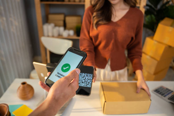 istock Close up hands of customer using mobile phone paying for goods package. Attractive handsome male customer making a easy and quick contactless payment for product from small business in warehouse store 1587039956