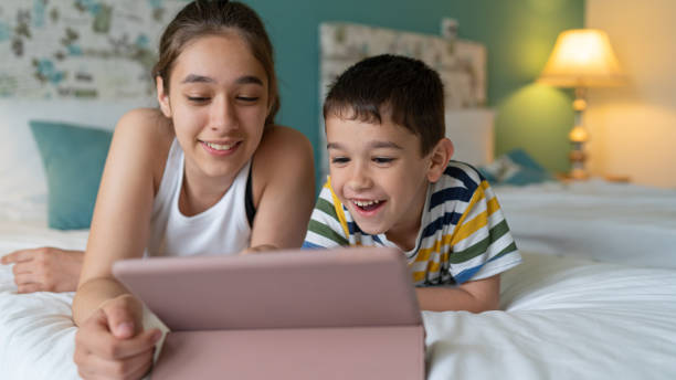 istock Happy brother and sister using digital tablet at home while laying down on a bed 1587056595