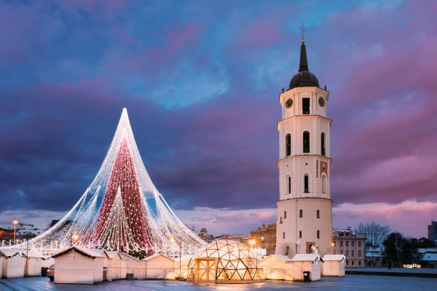 Vilnius, Lithuania. Amazing Magic Misty Cloud Colorful Sky Above Christmas Tree On Background. Bell Tower Belfry Of Vilnius Cathedral At Square In Evening New Year Christmas Xmas Illuminations