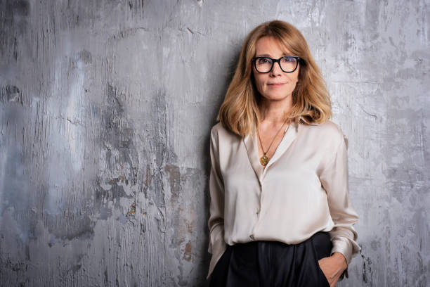 retrato de una mujer rubia de mediana edad parada frente a una pared gris - living room elegance women long hair fotografías e imágenes de stock