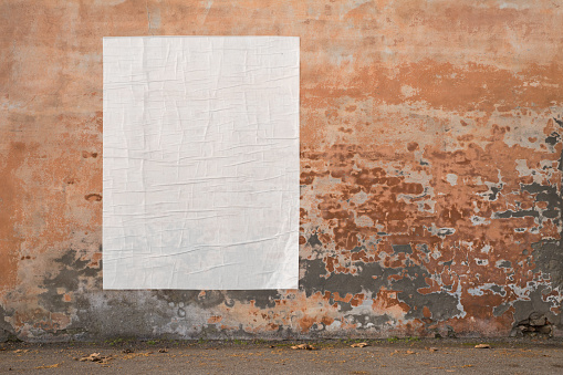 blank advertising poster glued to the weathered wall - copy space in pasted billboard on peeling plaster