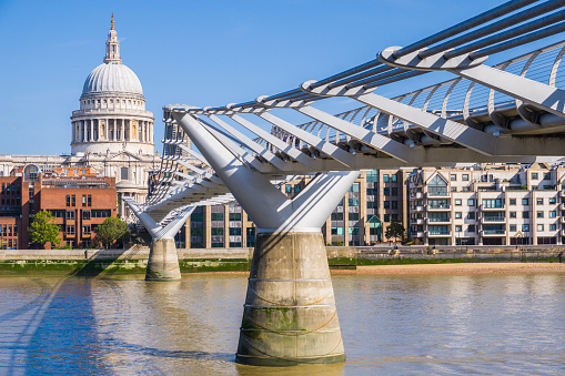 The futuristic glass and steel of the Millennium Bridge outside the Tate Modern spanning the River Thames at Bankside towards the iconic dome of St. Paul’s Cathedral in the City of London.