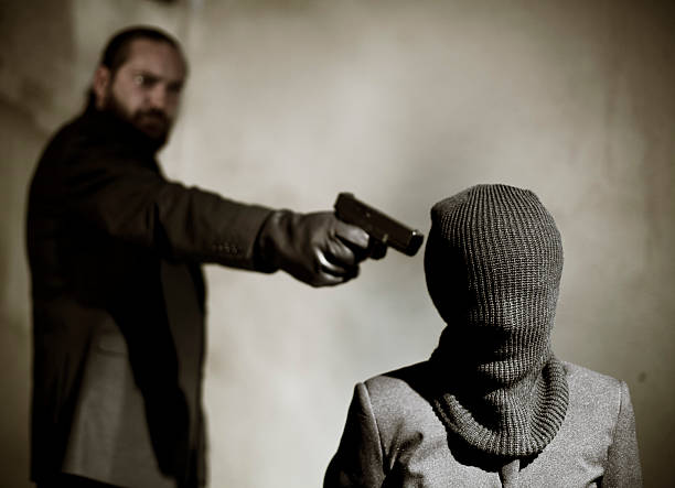 Bearded man pointing a gun at a man's temple to execute him