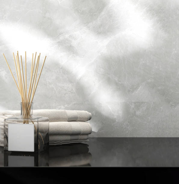 Reed stick diffuser in glass bottle, towel on black stone vanity counter top in sunlight on white marble wall