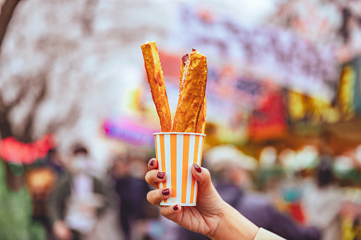 French fry or potato fries snack in a cup on asian woman hand with sakura cherry blossom festival background in Tokyo, Japan, Japanese local street food concept