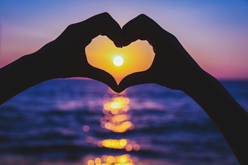 Female hands in heart shape on sea beach at sunset time background, Summer season