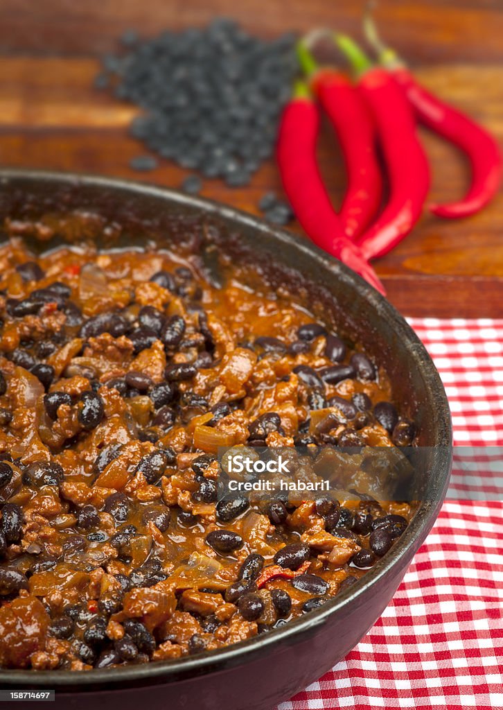 Chili con carne with black beans and red peppers Hot and spicy Chili con Carne in the frying pan with rice. Whole red peppers and raw black beans in the background. Black Bean Stock Photo