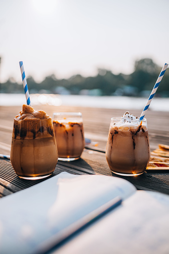 Three ice latte coffees on a wooden dock with a blurred beach background.