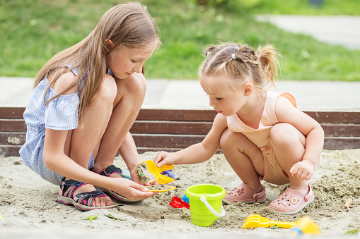 Girl and baby playing on sandbox. Toddler playing with sand molds and making mudpies. Outdoor creative activities for kids.