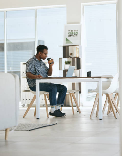 istock Black man, coffee drinking and office with laptop, table and thinking in marketing startup business. Man, drink espresso or tea at desk with computer, reading and planning for digital marketing job 1587182521