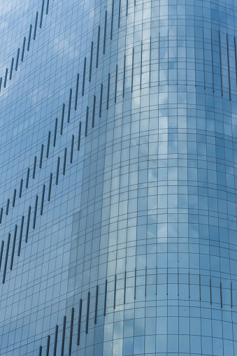 Facade of a multifaceted glass building and reflection of a blue sky with clouds on the mirrored surfaces of a modern building