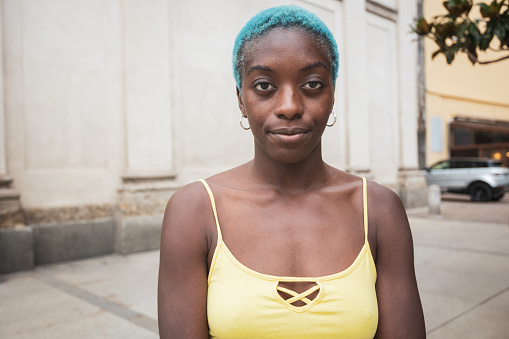 Portrait of a beautiful young African woman in a city looking at the camera. Cool attitude. Copy space. She has short hair colored in blue