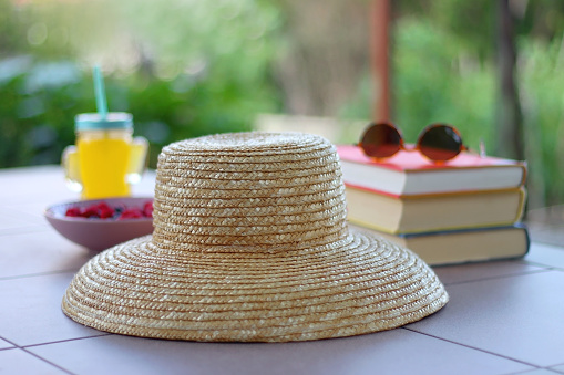 Straw hat, orange soda in the cactus shaped cup, bowl of fresh blueberreis and raspberries, plate of chocolate chip cookies, stack of books and sunglasses in the garden. Selective focus.