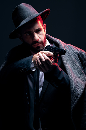 Bodyguard, suit or shooting gun on studio background in dark secret spy, isolated mafia leadership or crime lord security. Model, man and gangster aiming weapon in formal or fashion clothes aesthetic