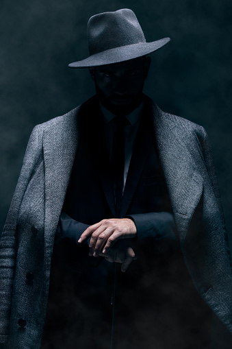 Mafia, fashion and mystery man in a suit isolated on a dark background in a studio. Business, vintage and stylish secret businessman for crime investigation, spy work and agent on a backdrop