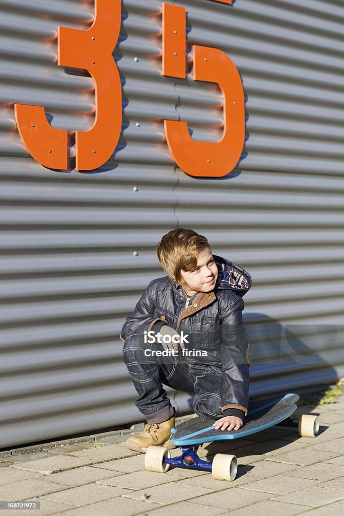 Skateboarder Portrait of boy crouching on a skateboard in front of metal fence 8-9 Years Stock Photo