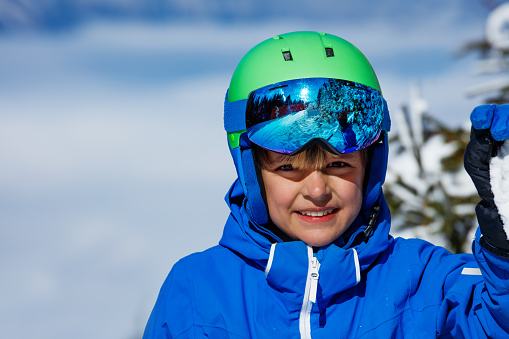 Close-up portrait of a happy young boy in ski helmet smile over sky