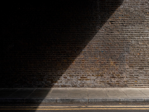 A diagonal beam of light cast on a wall underneath a railway bridge in East London
