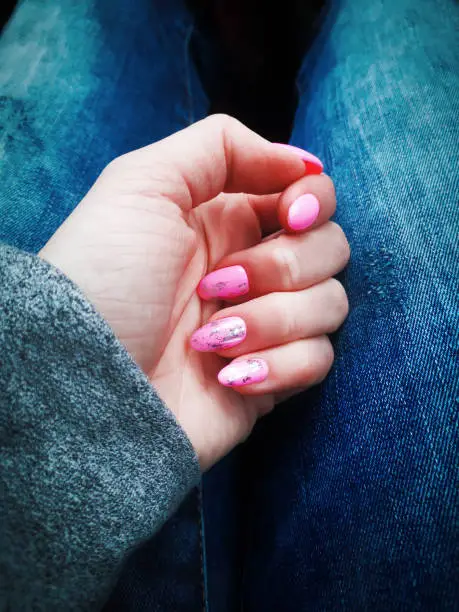 Manicure with pink varnish, complemented by design, on the hand of a young woman
