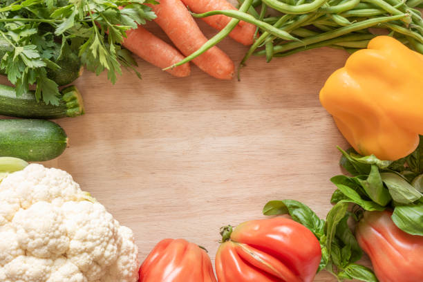 Fresh raw vegetables on a wood chopping board forming a frame with copy space