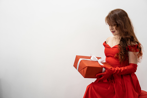 A young woman in red holds a beautifully decorated gift package, ready to surprise her loved ones on a special birthday. Isolate on white background. High quality photo