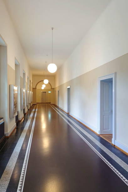 istock Long empty public building corridor or hallway. Wall and ceiling mounted light, no people 1587295224