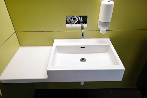 Public toilet washroom with a sink, faucet, and soap dispenser. Close up shot, no people.