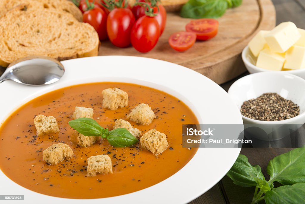 Cream of Tomato Soup Cream of tomato soup with croutons and cracked black pepper garnished with basil leaves. Sliced crusty bread and butter on background. Tomato Soup Stock Photo
