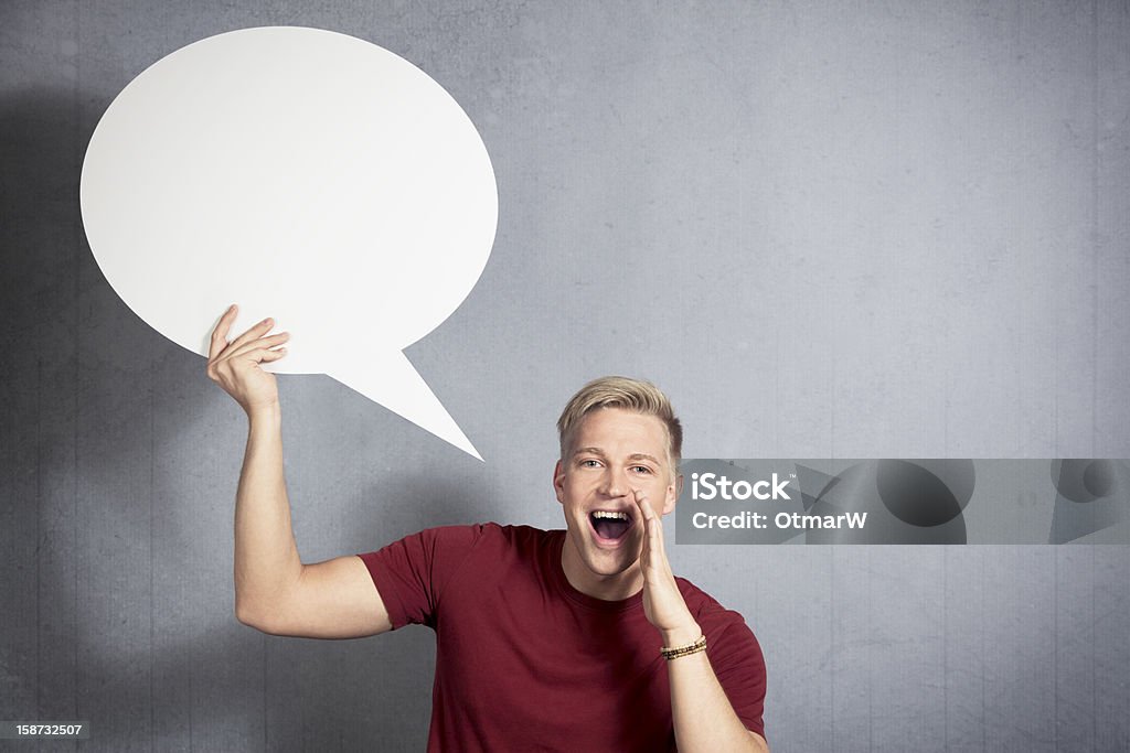 Happy man shouting fantastic news with speech ballon in hand. Fantastic news: Joyful man shouting great news while holding white blank speech bubble with space for text isolated on grey background. Adult Stock Photo