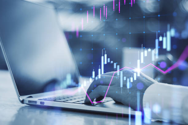 istock Close up of male hands using laptop keyboard at workplace with glowing candlestick forex chart on blurry background. Technology, trade and financial data concept. Double exposure. 1587360448