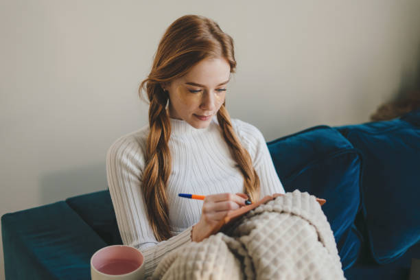 istock Young woman writing in notebook while sitting on sofa at home 1587381343