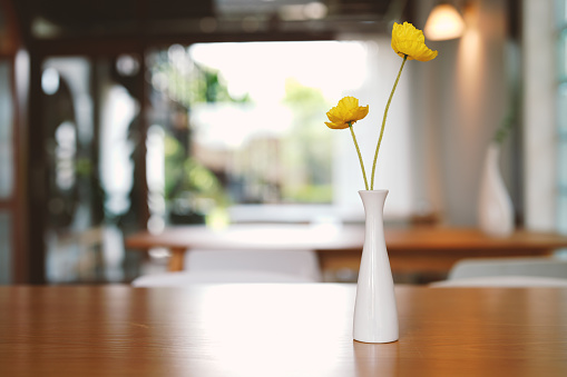 Yellow flowers in a white vase on wooden table in a cafe on blur background