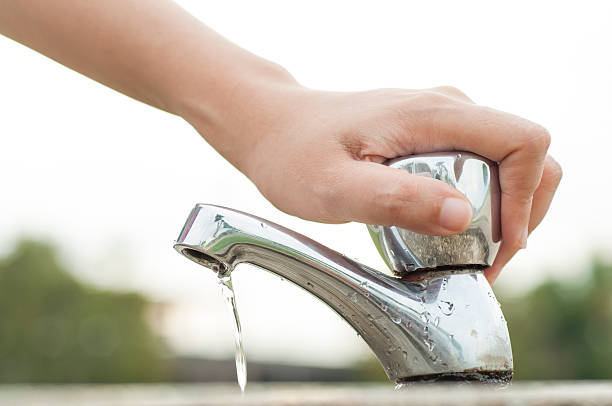 Hand tightly closing a water faucet outdoors stock photo