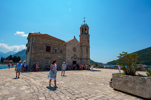 Church of Our Lady of the Rocks on the Island of Saint George, Bay of Kotor near Perast, Montenegro - June 27, 2023: a view of a tourists near the historic church, a bright sunny day, travel