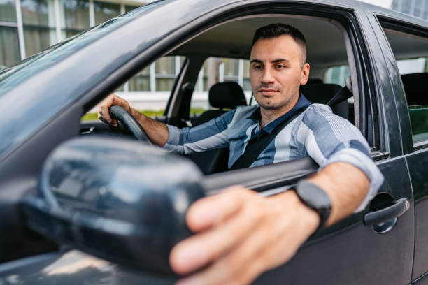 istock Young Man Adjusting His Side-View Mirror In The Car 1587404391