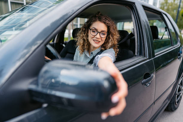 istock Young Woman Adjusting Her Side-View Mirror In The Car 1587407546