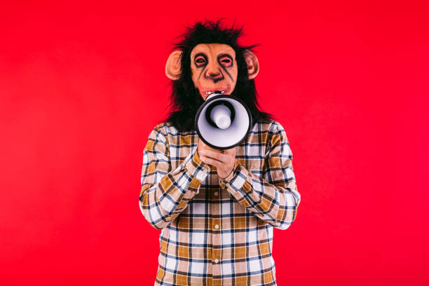 istock Man with chimpanzee monkey mask and plaid shirt, shouting with a megaphone, on red background. 1587414795