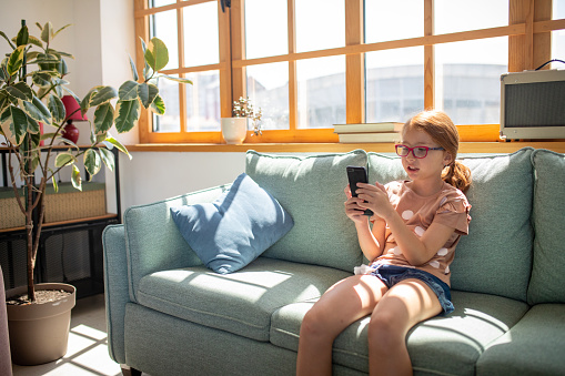 A young Caucasian girl using a smartphone in the living room of her apartment