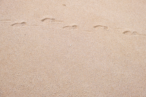 Foot prints on the sand , Beach scene . \nTexture background