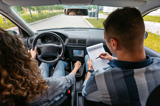 Young woman taking a driving test. A male driving instructor grading her using a checklist.