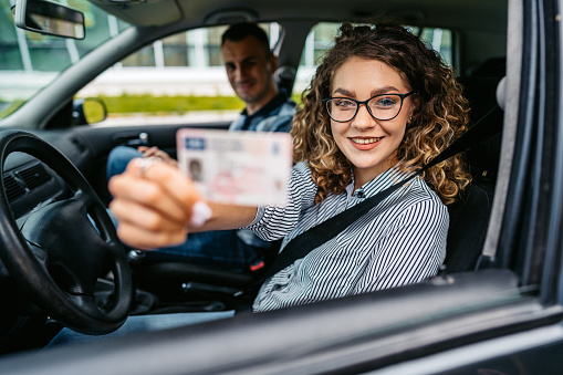 Portrait of a female student passing her driving test after a young driving instructor graded her. Holding her new driver's licence.