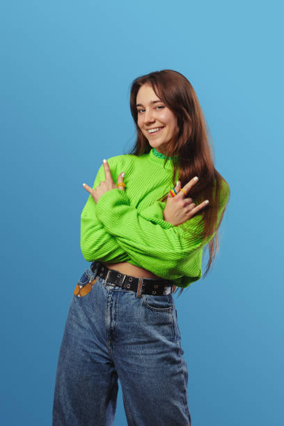 istock Young cute student girl, smiling brightly and looking at camera while showing rock and roll gesture. 1587458965