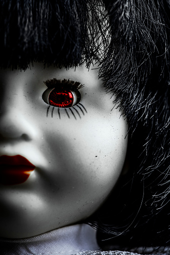 A close up of a creepy vintage doll with a glowing red eye.